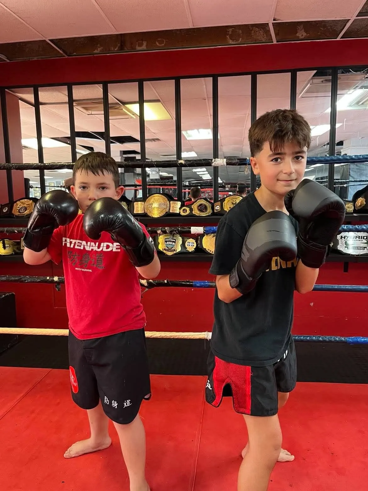 Deux jeunes de la classe enfants devant le ring et les ceintures de l'académie à Gatineau